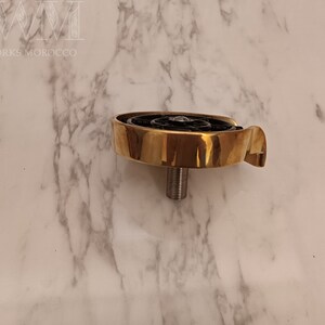 K&ouml;nnte beinhalten: Ein goldfarbener Metallhahn mit einem schwarzen, runden, dekorativen Element. Der Hahn hat einen Gewindestiel und einen gebogenen Auslauf.