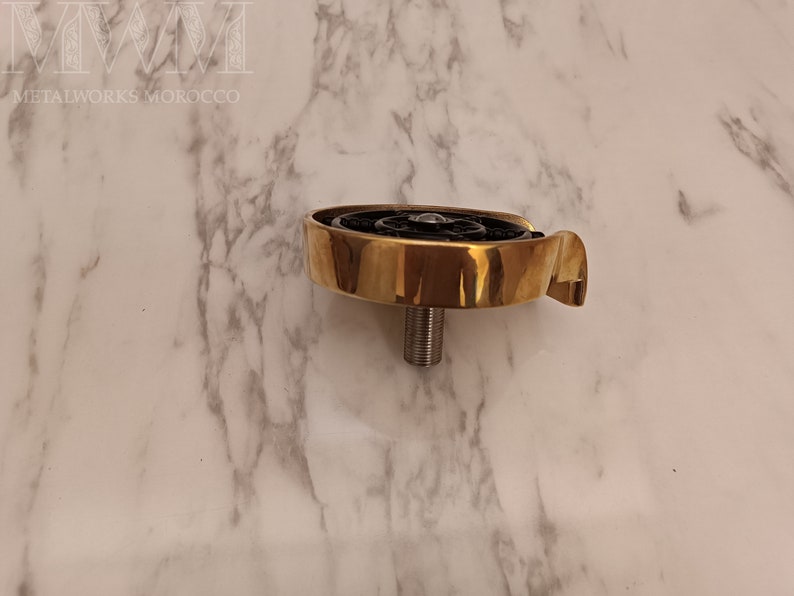 K&ouml;nnte beinhalten: Ein goldfarbener Metallhahn mit einem schwarzen, runden, dekorativen Element. Der Hahn hat einen Gewindestiel und einen gebogenen Auslauf.