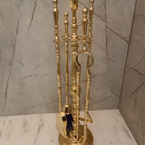 May include: A gold-toned fireplace tool set with a brush, shovel, poker, and tongs. The tools are mounted on a decorative stand with a hammered finish.
