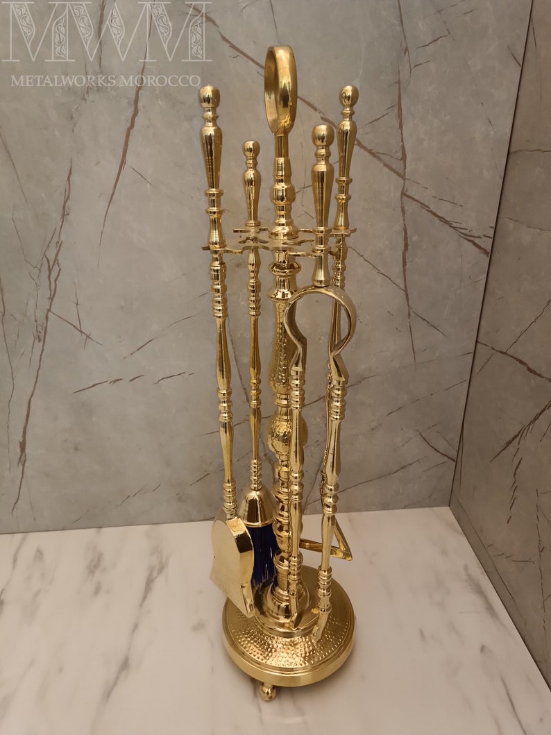 May include: A gold-toned fireplace tool set with a brush, shovel, poker, and tongs. The tools are mounted on a decorative stand with a hammered finish.