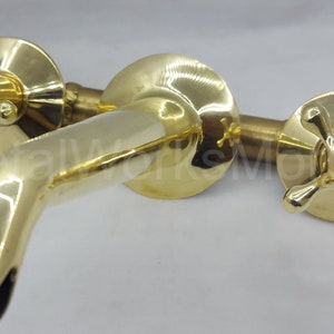 May include: A gold-toned, wall-mounted faucet with two cross-shaped handles. The faucet has a spout that curves downwards.