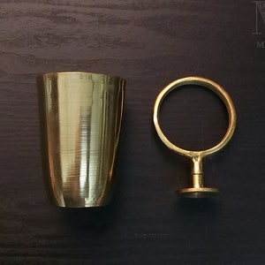 May include: A gold metal cup and a gold metal ring stand on a dark wood surface. The cup has a textured surface. The ring stand has a round top and a base.