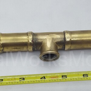 May include: Brass plumbing fitting with three sections, two of which are angled, and a centre section with a T-shaped connector. The fitting is 17.8 cm long and has a 1.27 cm diameter.