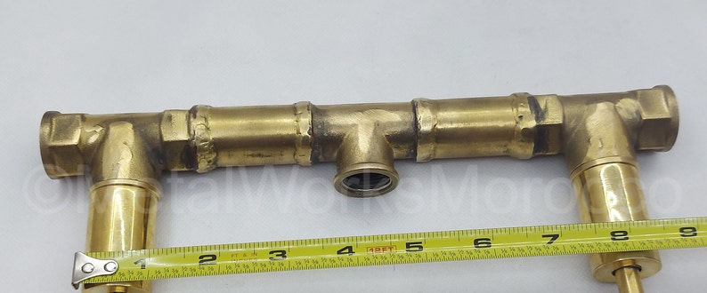 May include: Brass plumbing fitting with three sections, two of which are angled, and a centre section with a T-shaped connector. The fitting is 17.8 cm long and has a 1.27 cm diameter.