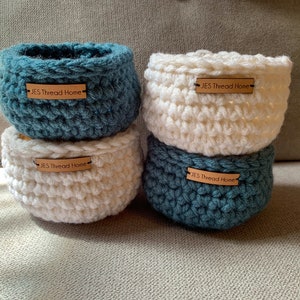 May include: Four crocheted baskets, two white and two blue, with brown labels that read "JES Thread Home".