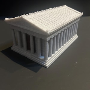 May include: A small, grey model of a classical temple. The structure has a rectangular base, vertical columns along the sides, and a sloped roof. The architectural model is a detailed representation of ancient Greek design.