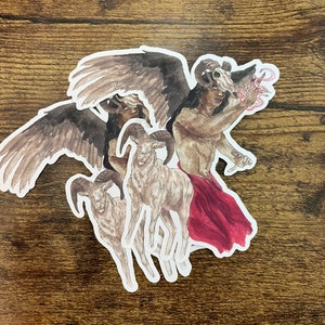 Könnte beinhalten: Eine Sammlung von Aufklebern mit Aquarellillustrationen einer geflügelten Figur mit einem Widder-Schädel, einem Widder und einer Figur mit rotem Tuch. Die Aufkleber haben einen weißen Rand und befinden sich auf einer Holzoberfläche.