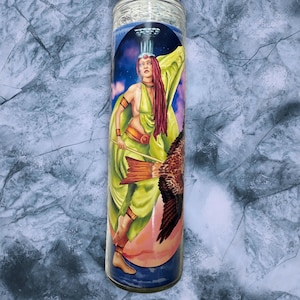 Peut inclure: Une bougie en verre avec une illustration colorée d'une femme en robe verte, tenant un bâton et accompagnée d'un oiseau. Le fond présente un ciel nocturne et un globe rose et bleu.