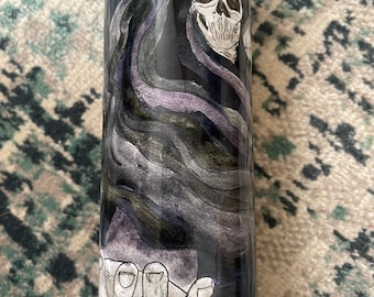 May include: A black candle with a white illustration of a skeletal figure wearing a hooded robe. The figure is holding out its hand with its fingers extended.