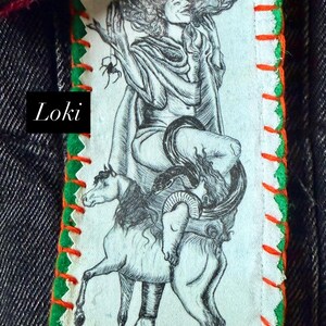 May include: A rectangular patch with a black and white illustration of a figure riding a horse-like creature, with a snake wrapped around it. The patch has green and orange stitching and the word "Loki".