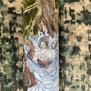 May include: A green glass candle with a watercolour illustration of figures in a forest. The artwork features a woman with flowing hair and a flowing blue gown, and other figures in brown cloaks. The candle has a tree and forest scene.
