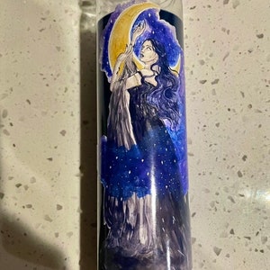 Puede incluir: Un portavelas de vidrio con base negra y una imagen colorida de una mujer con cabello largo y oscuro que alcanza una luna creciente. El fondo es azul oscuro con estrellas blancas y nubes.