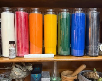 May include: A wooden shelf is filled with a rainbow of candles in glass jars, alongside small bottles, a mortar and pestle, and a jar marked "MINT". The display suggests a collection of spiritual or decorative items, with a focus on colour.