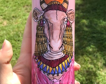May include: Pink candle with a hand-drawn illustration of a cow wearing a crown and jewelry. The cow has a pink nose and brown eyes.