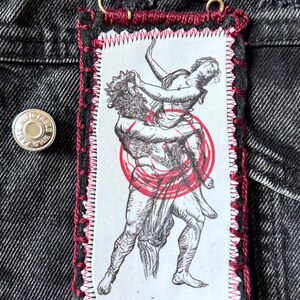 May include: A rectangular patch featuring a black and white illustration of Hades carrying Persephone, with a red circle overlay. The patch is sewn with red thread and has the text "Hades and Persephone".
