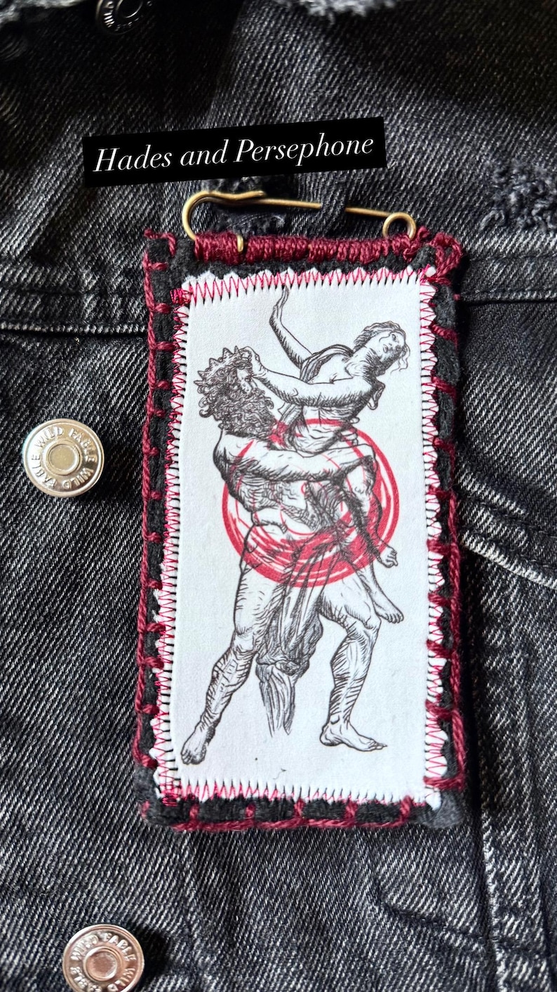 May include: A rectangular patch featuring a black and white illustration of Hades carrying Persephone, with a red circle overlay. The patch is sewn with red thread and has the text "Hades and Persephone".