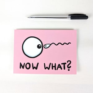 Op de afbeelding: Een roze kaart met een cartoon oog- en sperma-illustratie, met de tekst "NOW WHAT?" in het zwart. Een zwarte en doorzichtige pen is boven de kaart geplaatst. De kaart ligt op een witte ondergrond.