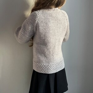 May include: A light gray knitted sweater with long sleeves and a ribbed hem. The sweater is made of a soft, comfortable material.