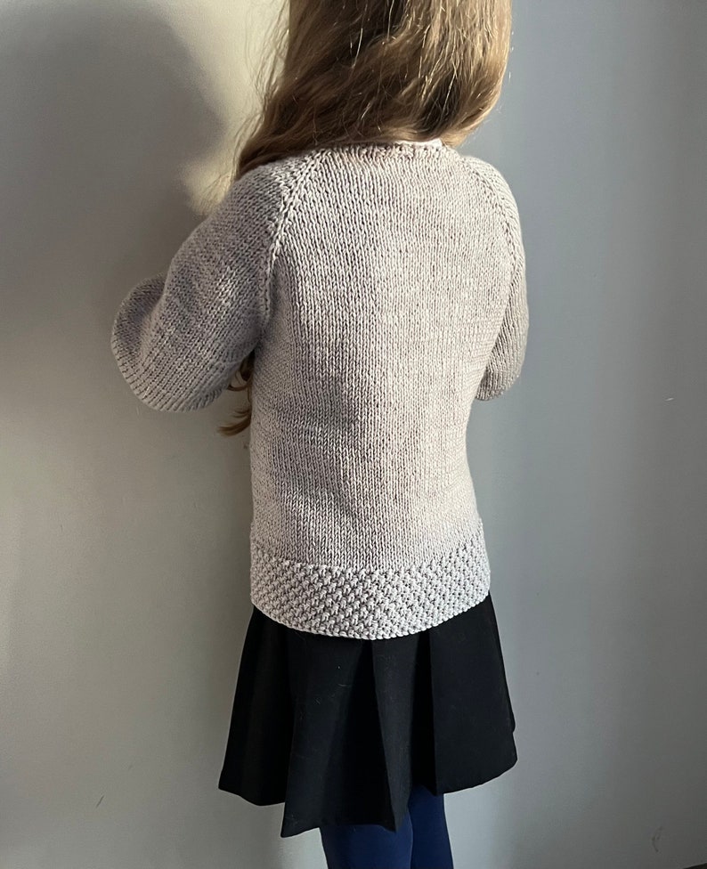 May include: A light gray knitted sweater with long sleeves and a ribbed hem. The sweater is made of a soft, comfortable material.