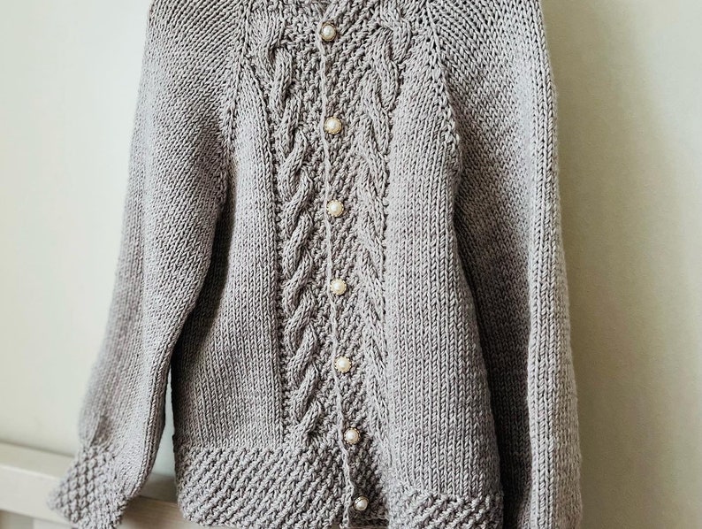 May include: A gray knitted cardigan with a cable knit pattern and pearl buttons.
