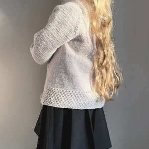 May include: A light pink knitted cardigan with a ribbed texture and a black pleated skirt.