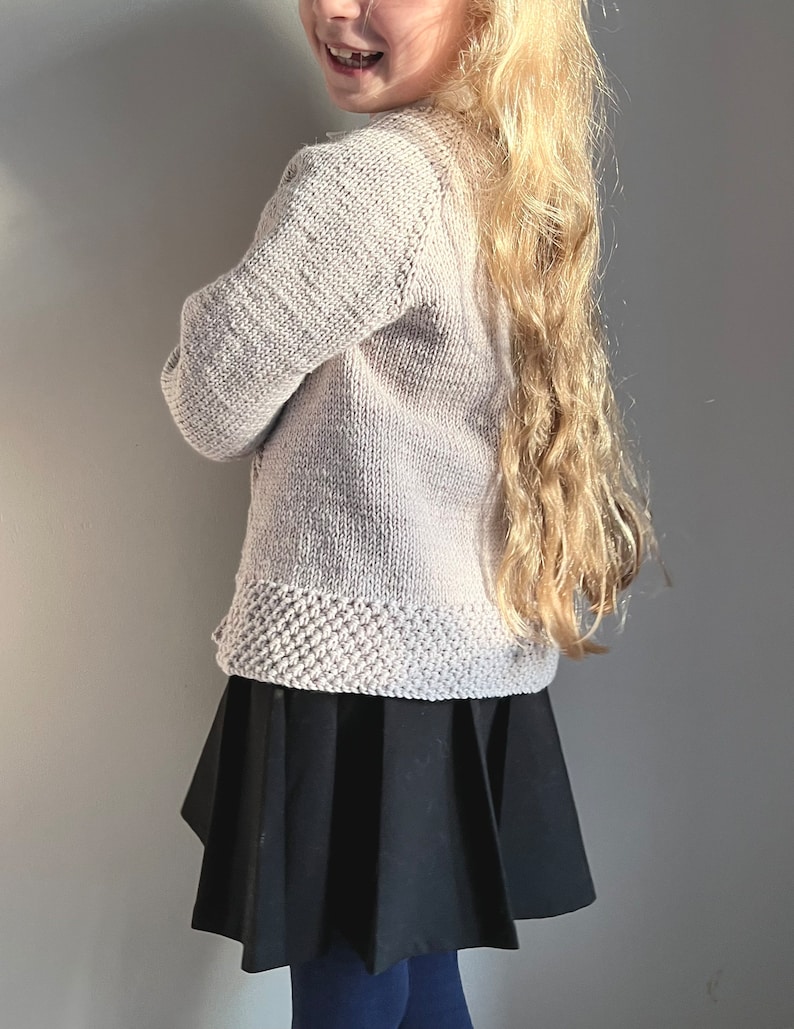 May include: A light pink knitted cardigan with a ribbed texture and a black pleated skirt.