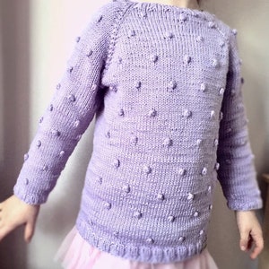 May include: A lavender knitted sweater with a textured pattern of small raised dots. The sweater has long sleeves and a round neckline.