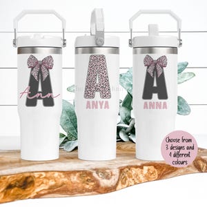 May include: White insulated tumblers with a handle, featuring a bow and initial design. The tumblers have a silver lid and handle. The text on the tumblers includes names like "Anna" and "Anya". The image also includes the text "Choose from 3 designs and 4 different colours".