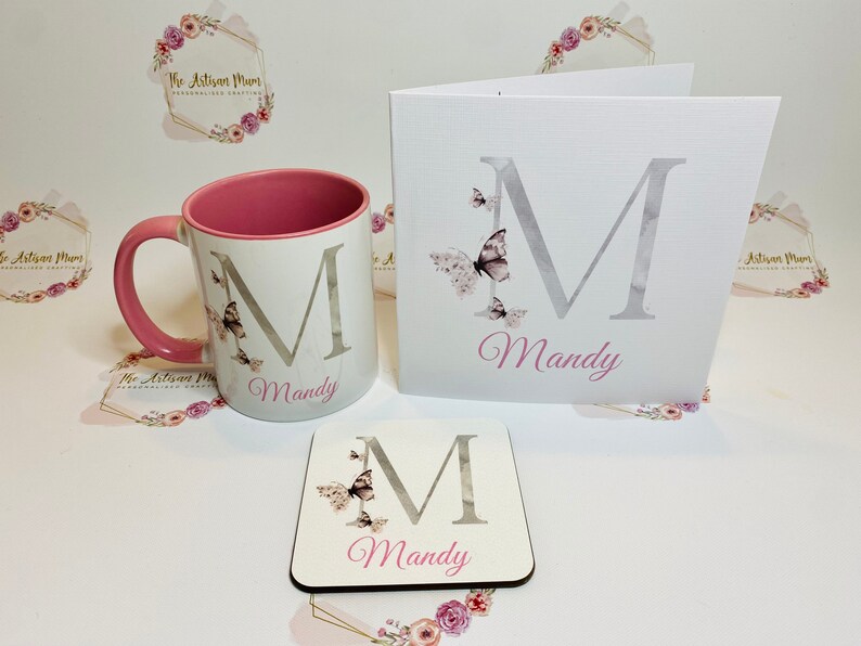 Puede incluir: Un conjunto de regalo personalizado que incluye una taza blanca con borde rosa, un posavasos y una tarjeta. Todos los art&iacute;culos presentan una letra "M" plateada con mariposas y el nombre "Mandy" en letras rosas.