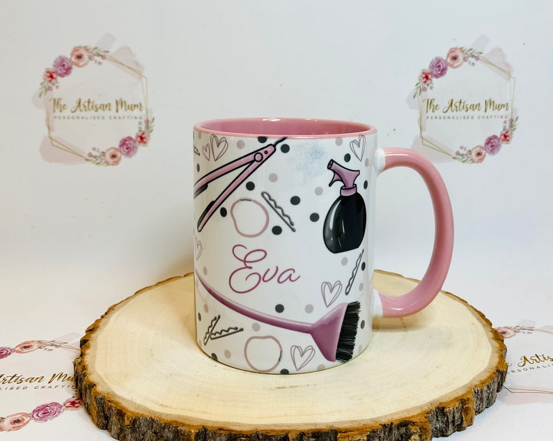 Peut inclure: Une tasse en c&eacute;ramique rose et blanche avec une anse rose. La tasse est d&eacute;cor&eacute;e d'outils de coiffure, notamment des ciseaux, une brosse &agrave; cheveux, un flacon pulv&eacute;risateur et des pinces &agrave; cheveux. Le nom "Eva" est &eacute;crit en rose sur la tasse.