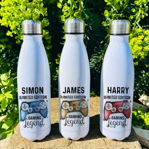 May include: Three white stainless steel water bottles with a gamer theme. The bottles have different names on them: Simon, James, and Harry. Each bottle has a different coloured controller graphic with the text "Limited Edition" and "Gaming Legend".
