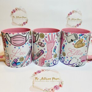 May include: Three pink mugs with white handles. Each mug has a different design featuring medical supplies and the names Lou, Ellie, and a third name that is unclear. The mugs are on a white surface with a floral design.