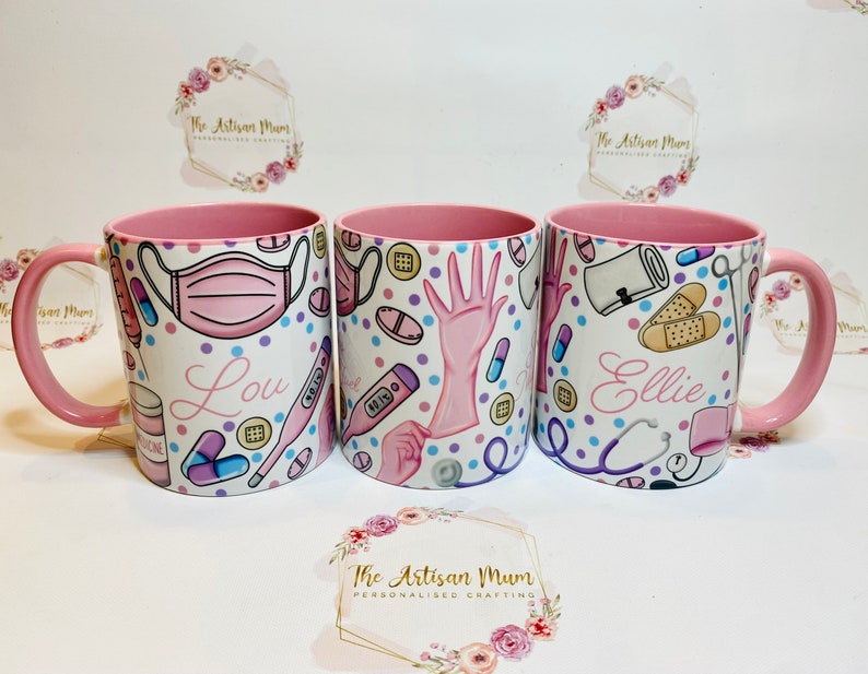 May include: Three pink mugs with white handles. Each mug has a different design featuring medical supplies and the names Lou, Ellie, and a third name that is unclear. The mugs are on a white surface with a floral design.