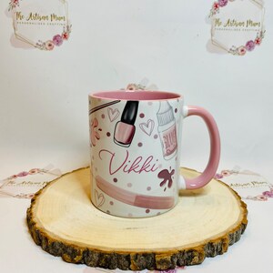 Pu&ograve; includere: Una tazza in ceramica bianca con un bordo e un manico rosa. La tazza ha un design rosa e bianco con smalto per unghie, cuori e la parola "Vikki".