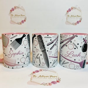 Peut inclure: Trois tasses en c&eacute;ramique rose et blanche avec un bord rose. Chaque tasse porte un nom diff&eacute;rent&nbsp;: Sophie, Leah et un nom illisible. Les tasses sont d&eacute;cor&eacute;es d&rsquo;un motif noir et blanc d&rsquo;outils de coiffure, notamment des peignes, des brosses et des lisseurs.