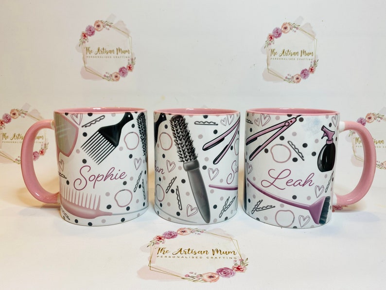 Peut inclure: Trois tasses en c&eacute;ramique rose et blanche avec un bord rose. Chaque tasse porte un nom diff&eacute;rent&nbsp;: Sophie, Leah et un nom illisible. Les tasses sont d&eacute;cor&eacute;es d&rsquo;un motif noir et blanc d&rsquo;outils de coiffure, notamment des peignes, des brosses et des lisseurs.