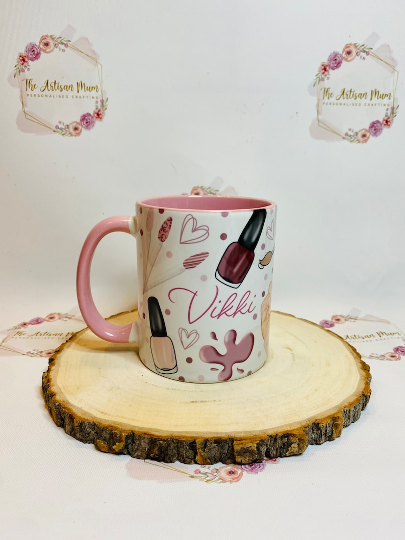 Pu&ograve; includere: Una tazza in ceramica rosa e bianca con un manico rosa. La tazza ha un design di bottiglie di smalto per unghie, cuori e schizzi di vernice rosa. Il nome "Vikki" &egrave; scritto in un font rosa su la tazza.