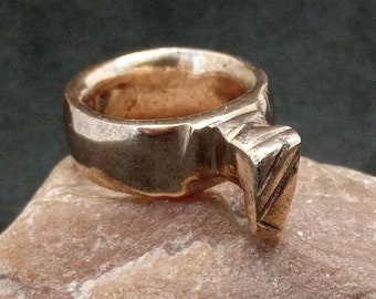 May include: A gold-colored ring with a hammered finish and a raised, triangular design on the top.