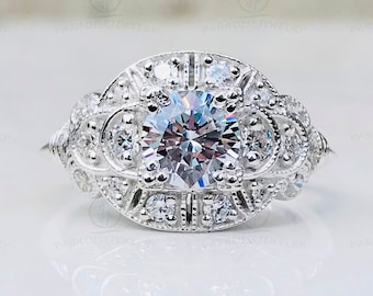 May include: A silver engagement ring with a large, round, clear center stone. The ring features intricate detailing with smaller accent stones and a decorative setting. The ring is set against a white background.