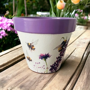 May include: A purple and white ceramic flower pot with a bee and floral design.