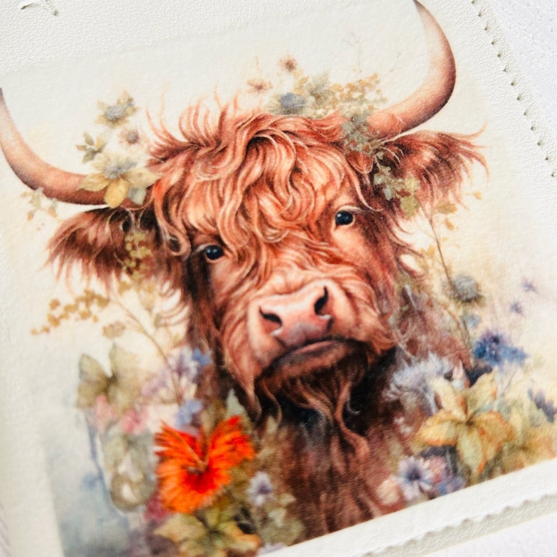Pu&ograve; includere: Un primo piano di una mucca Highland marrone e bianca con pelo lungo e irsuto. La mucca &egrave; circondata da una variet&agrave; di fiori selvatici, tra cui fiori arancioni, blu e bianchi.