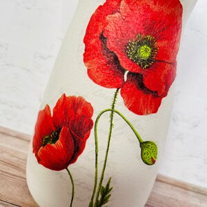 May include: White ceramic vase with a red poppy flower design. The vase has a textured surface and a narrow neck.