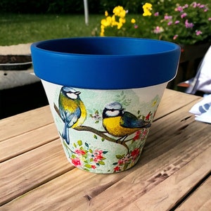 May include: Blue and white ceramic planter with a floral design and two bluebirds. The planter has a blue rim.