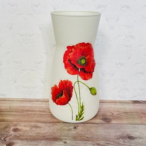 May include: White ceramic vase with a floral design featuring two red poppies. The vase has a textured surface and a slightly flared opening.