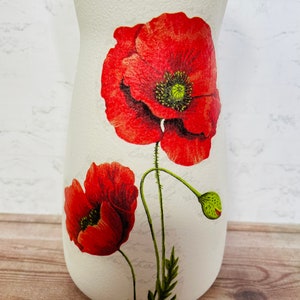 May include: White ceramic vase with a floral design featuring red poppies. The vase has a textured surface and a narrow neck.