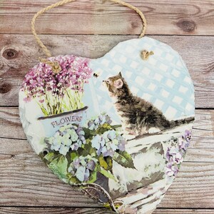 K&ouml;nnte beinhalten: Eine herzf&ouml;rmige Schiefertafel mit blau-wei&szlig;em kariertem Hintergrund. Die Tafel zeigt ein Blumenmuster mit einer Katze, die eine Biene betrachtet, und den Text "FLOWERS".