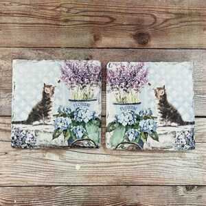 May include: Two square decorative tiles with a vintage design. Each tile features a kitten, lavender, and blue hydrangeas. The word "FLOWERS" is printed on the pots. The background has a light blue trellis pattern.