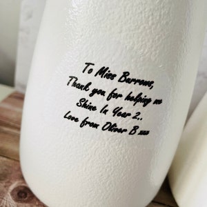 May include: White ceramic vase with a handwritten message that reads "To Miss Burrows, Thank you for helping me Shine In Year 2.. Love from Oliver B xus".