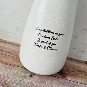 May include: White ceramic vase with black handwritten text that reads "Congratulations on your New home Nade. So proud of you.. Frankie & Ollie xxx"