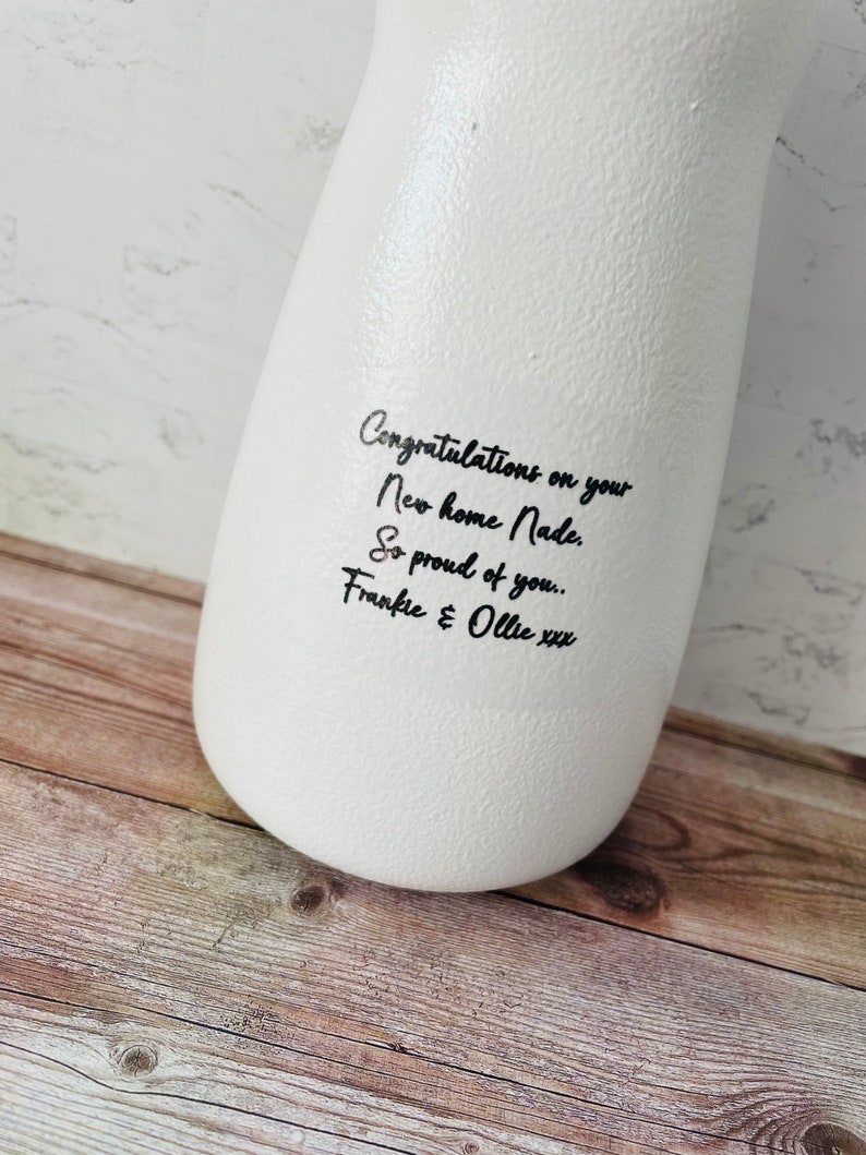 May include: White ceramic vase with black handwritten text that reads "Congratulations on your New home Nade. So proud of you.. Frankie & Ollie xxx"
